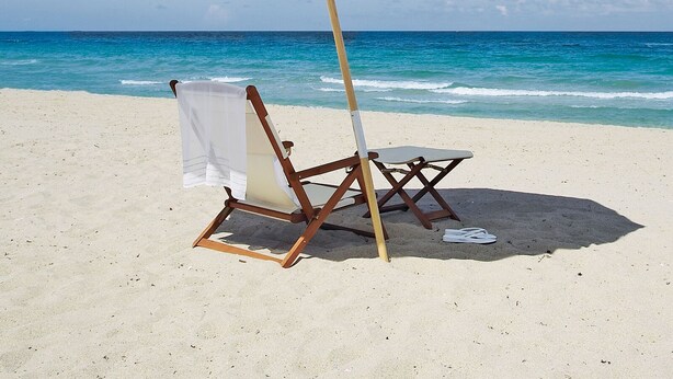 A beach umbrella, a beach chair, and a beach towel on a sandy beach with the ocean in the background. - THE OCEAN VILLA (Matara)