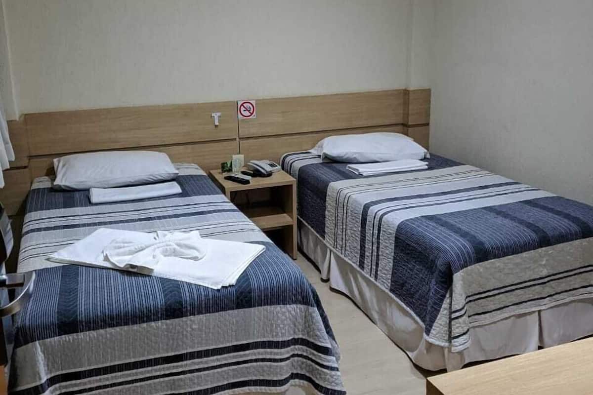 A hotel room with two beds, each with striped bedding and pillows. There is a wooden headboard, a bedside table with a phone, and a no-smoking sign on the wall.
