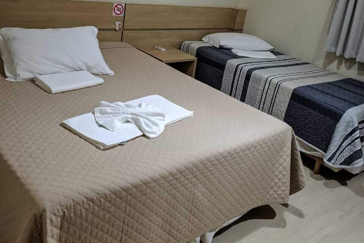 A hotel room with a large bed, two smaller beds, a nightstand, and a sign indicating no smoking.