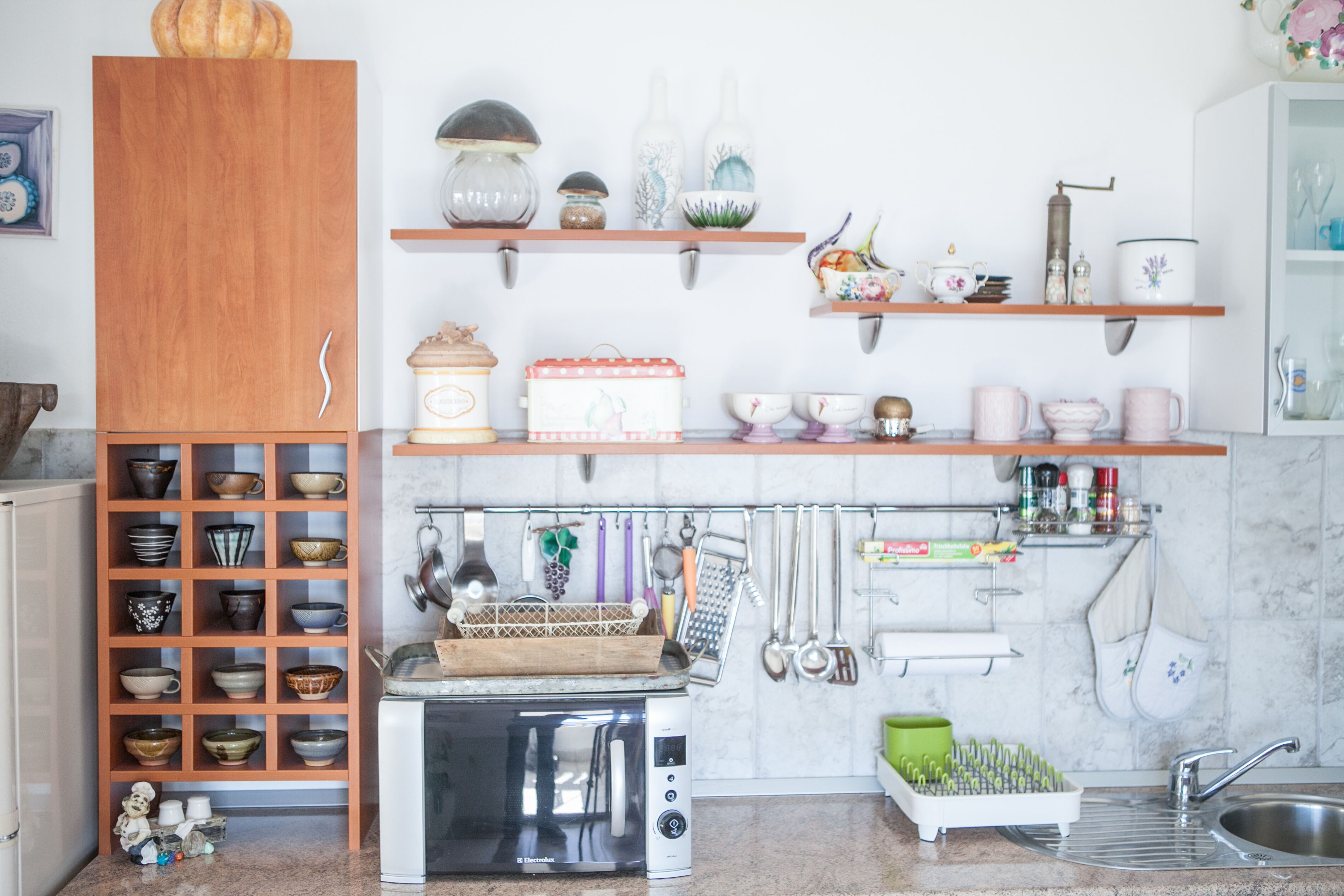 A kitchen with wooden shelves, a microwave, and various utensils.