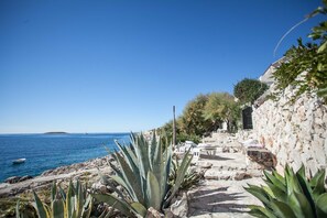 A coastal area with a stone pathway leading to a seating area with white chairs and tables, overlooking the sea. - Sevid Holiday Homes (Marina)