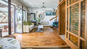 Ein großzügiger Wohnbereich mit Holzboden, einem grünen Sofa, einem kleinen Tisch mit weißer Spitzenauflage und einer Treppe, die zu einer oberen Ebene führt.