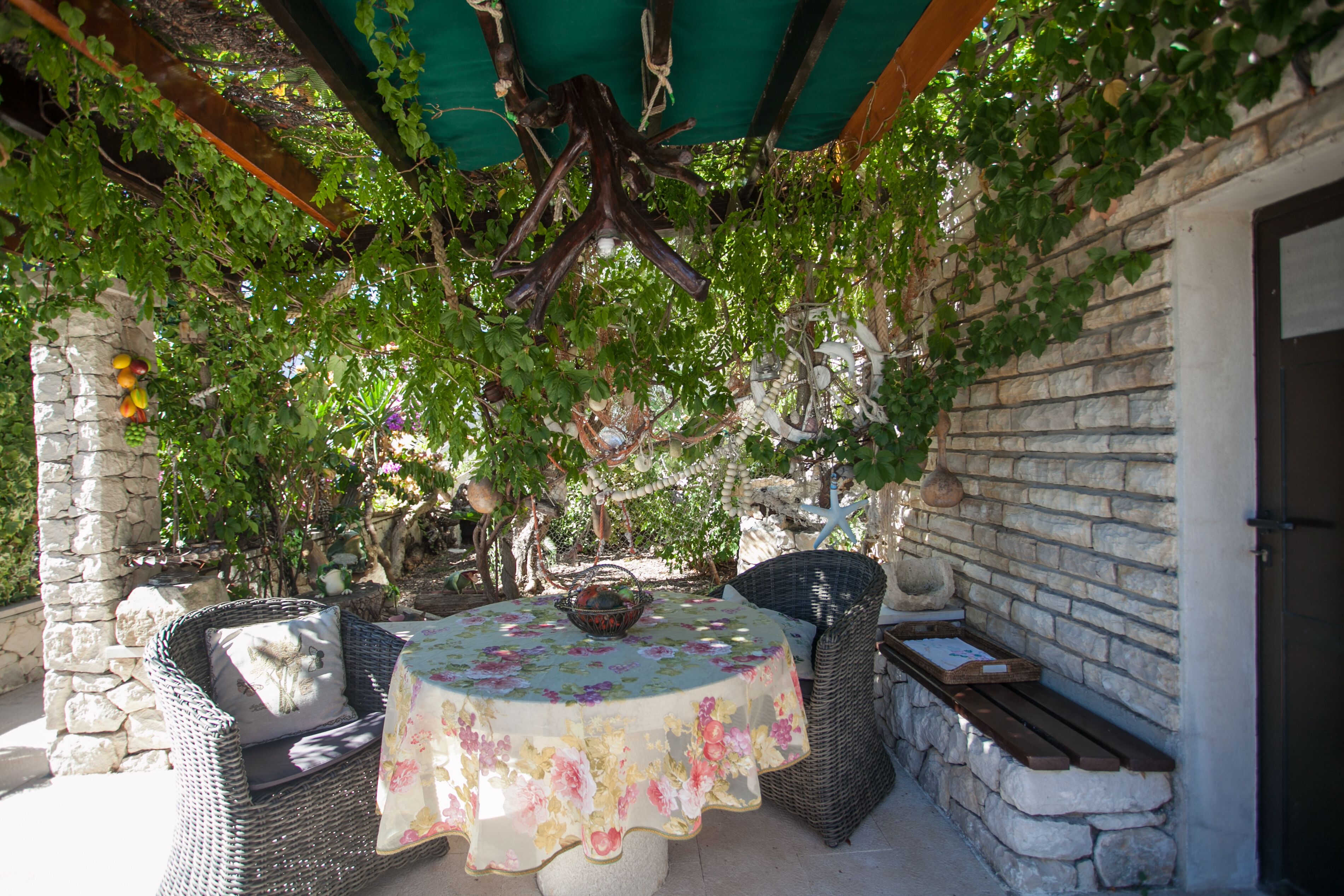 An outdoor patio with wicker furniture, a round table with a floral tablecloth, and a stone wall.