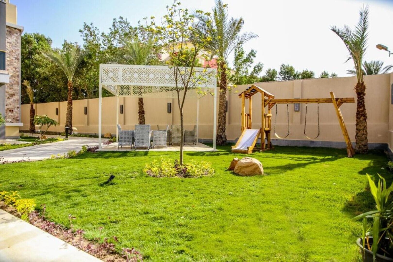 A well-maintained backyard with a swing set, a small slide, and a seating area with chairs.