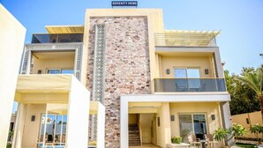 A modern multi-story hotel with a central tower, balconies, and a swimming pool. - Three-Bedroom Apartment Serenity Home Hurghada 03 (Hurghada)