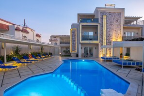 Un hotel moderno con piscina, tumbonas y fachada bien iluminada.