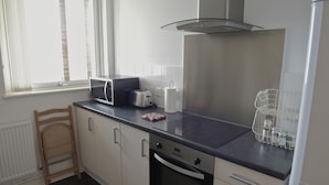 Una cucina moderna con forno integrato, microonde e tostapane. Si nota una sedia in legno e un termosifone bianco.