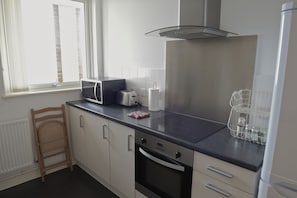 Een moderne keuken met een ingebouwde oven, een magnetron en een broodrooster. Er staat een houten stoel en er is een witte radiator.
