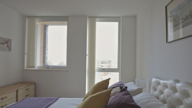 Una camera da letto con un letto, due finestre, un comodino e un quadro appeso al muro.