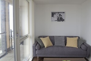 A living room with a grey sofa, two yellow cushions, and a poster on the wall.
