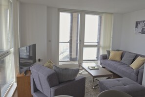 Een moderne woonkamer met een grijze bank, een salontafel en een flatscreen televisie op een houten standaard.
