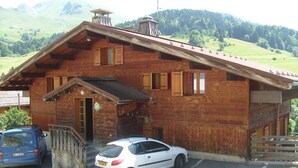 A wooden lodge with a sloped roof, a front entrance, and a car parked in front. - Spacious Savoyard chalet apt, equipped kitchen, 4 bedrooms, 2 baths, Le Chinaillon (Le Grand-Bornand)