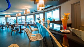 A modern restaurant with a bar area, large windows offering a view, and a variety of seating options. - Casa Mia Family Suite (Agadir)