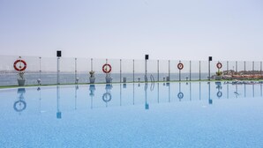 A clear blue pool with lifebuoys and speakers along the edge, overlooking a rocky coastline. - Casa Mia Family Suite (Agadir)