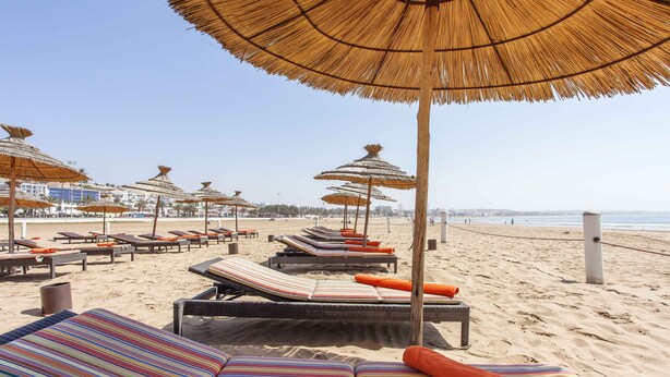 A beachside lounge area with striped cushions and thatched umbrellas. - Casa Mia Family Suite (Agadir)