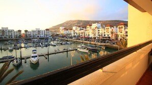 A marina with boats docked, a mountain in the background, and buildings with red roofs. - Casa Mia Family Suite (Agadir)