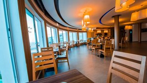 A spacious restaurant with wooden furniture and large windows offering a view of the cityscape. - Casa Mia Family Suite (Agadir)