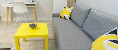 A modern living room with a grey sofa, a yellow table, and a white desk with a chair.