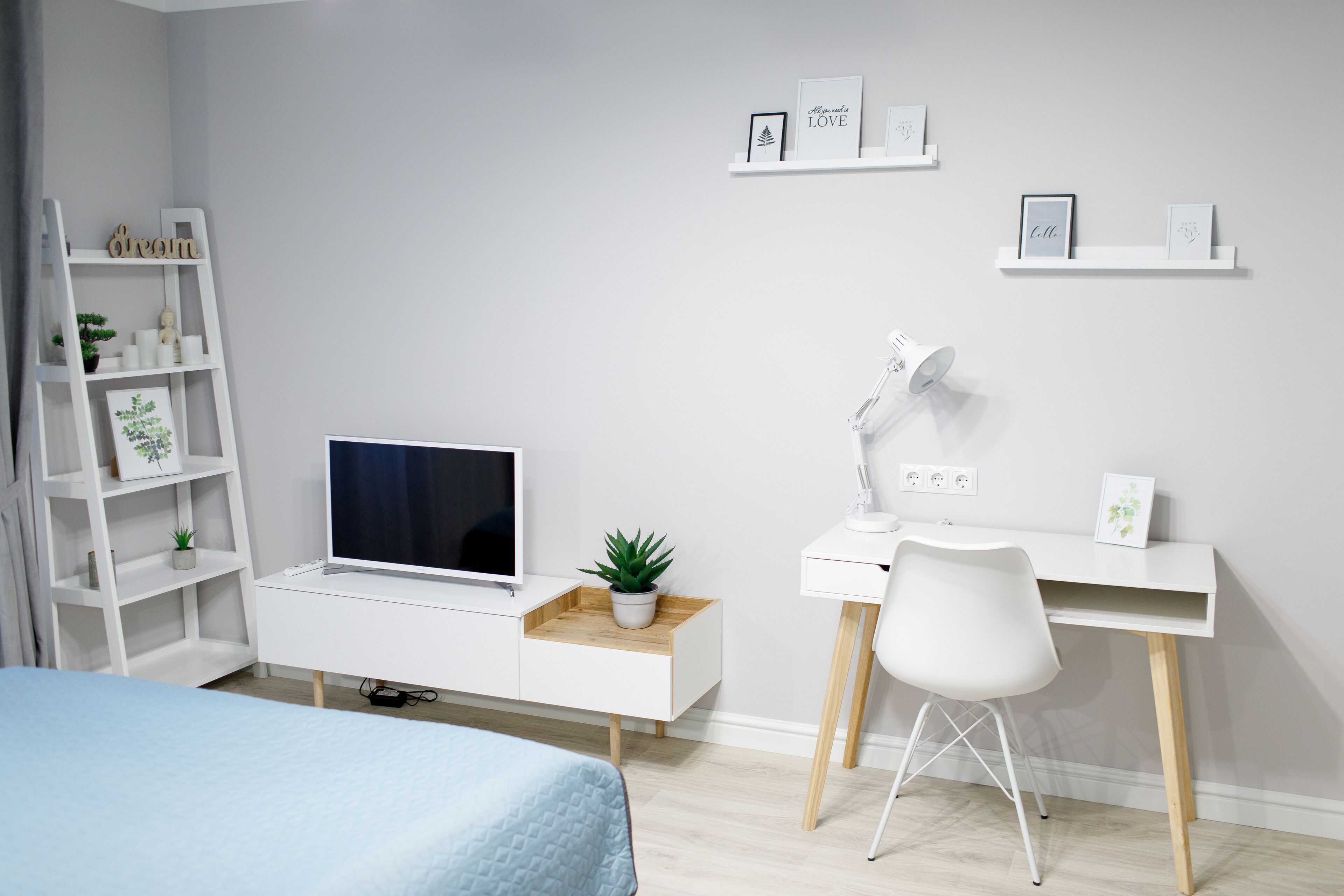A modern bedroom with a bed, a desk with a chair, a TV, and a shelf with decorative items.