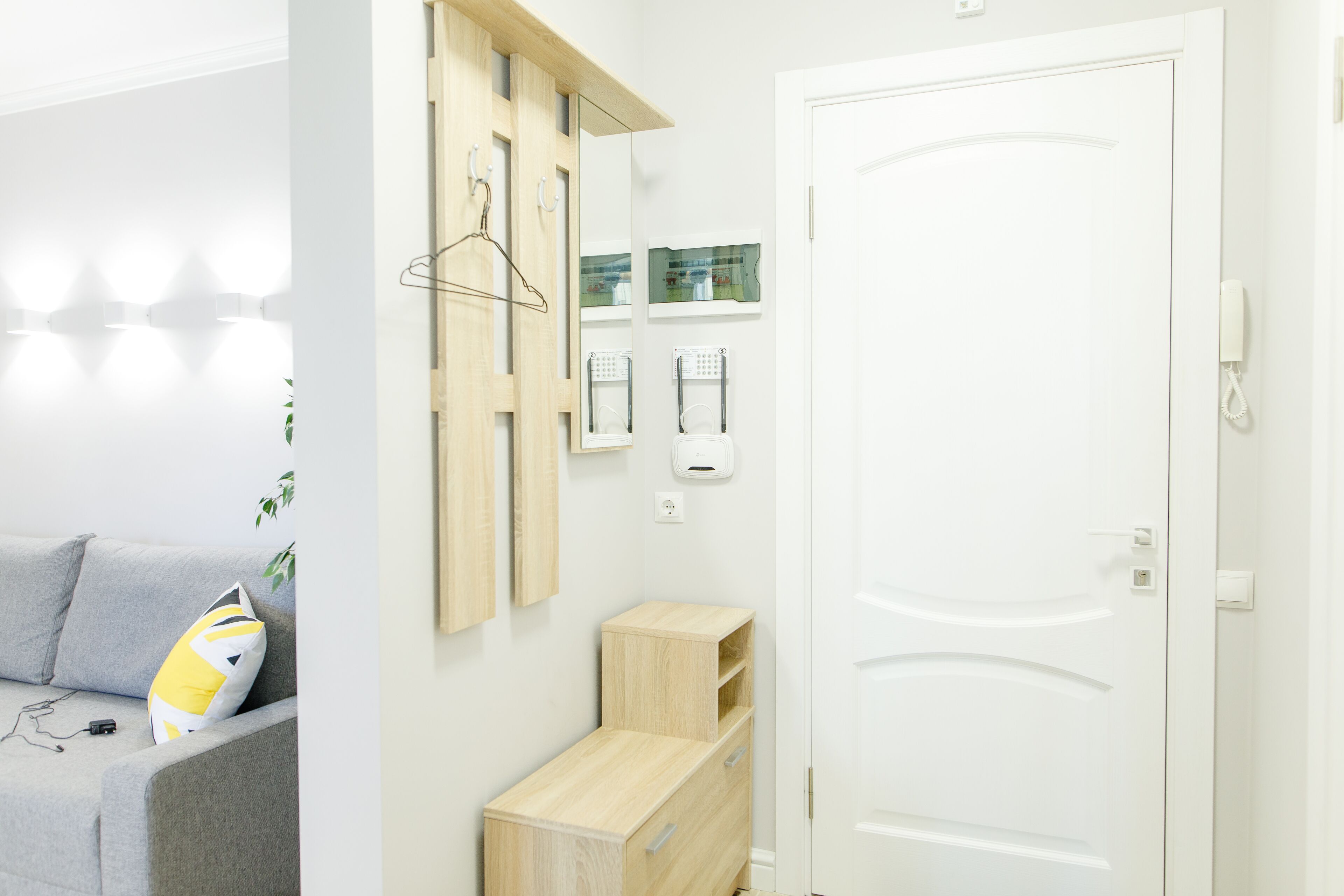 A modern room with a grey sofa, a wooden cabinet, a white door, and a wall-mounted mirror.