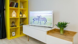 Una sala de estar moderna con un mueble blanco para entretenimiento, una estantería amarilla y un televisor de pantalla plana mostrando cebras.