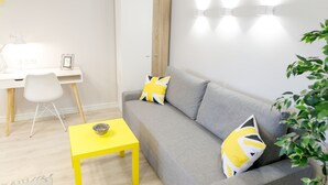 Una sala de estar moderna con un sofá gris, almohadas amarillas y blancas, una mesa amarilla, un escritorio blanco con una silla y un armario.