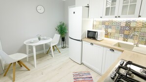 Cocina compacta con gabinetes blancos, microondas, estufa y comedor con una mesa y sillas pequeñas.