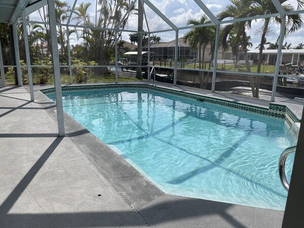 A swimming pool with a tiled edge, surrounded by a covered area with metal beams. - 3BD/3BA w/Electric Dock/Heated Pool; SUMMER VACA; Gulf Access – BUDGET FRIENDLY! (Cape Coral)