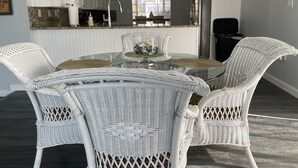 Una cocina moderna con armarios blancos, un refrigerador de acero inoxidable y un comedor con una mesa de vidrio rodeada de sillas de mimbre.
