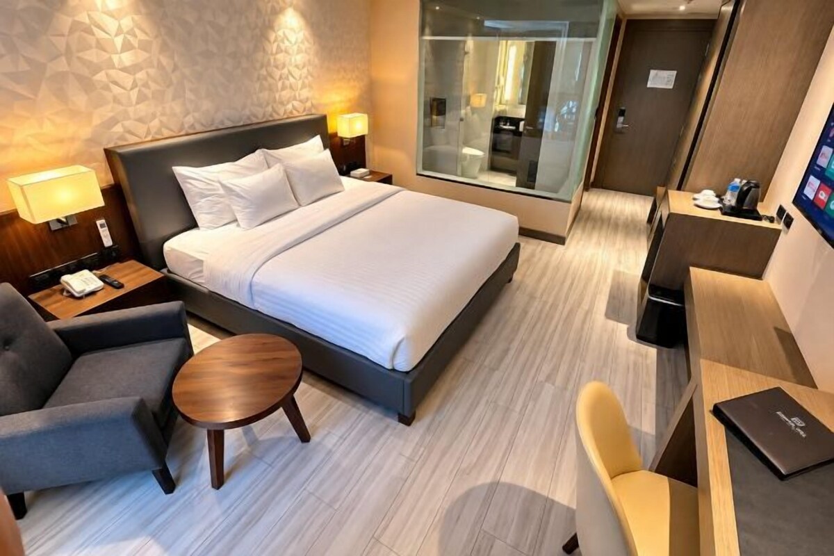 Una habitación de hotel con una cama, mesitas de noche, un escritorio, una silla y una pequeña mesa redonda.