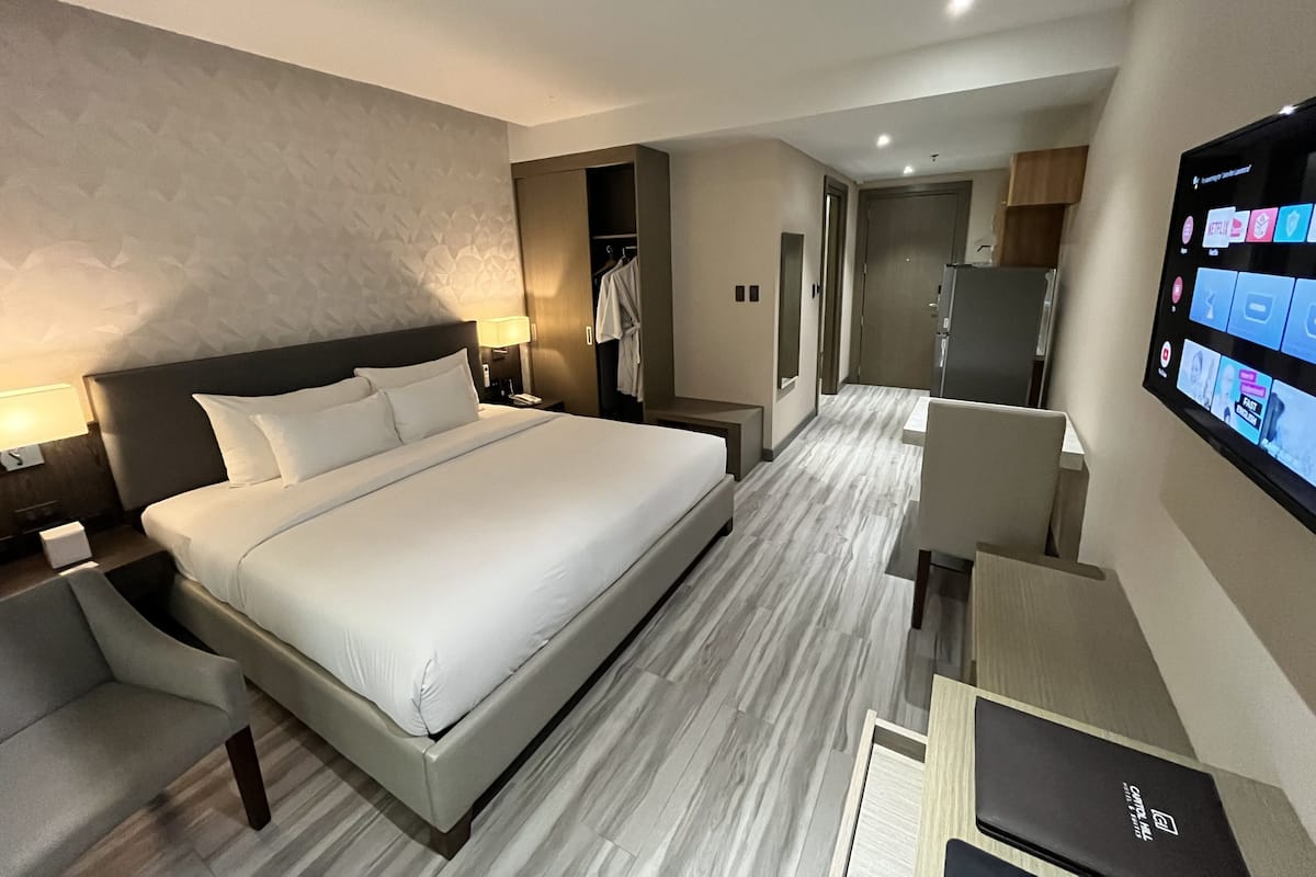 A modern hotel room with a large bed, a desk, a television, and a wardrobe.