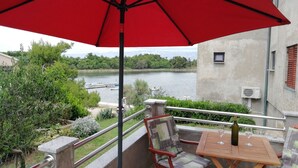 A balcony with a red umbrella, a wooden table with a bottle and glasses, and a view of a lake with boats. - Studio apartment in Nin with Seaview, Terrace, Air condition, WIFI (4868-1) (Nin)