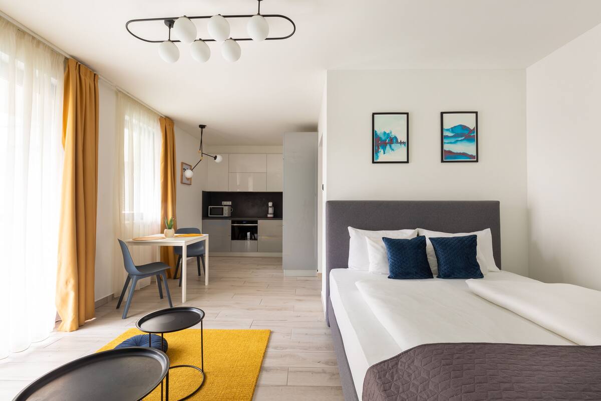 Una habitación de hotel moderna con una cama, un área de comedor y una cocina al fondo.