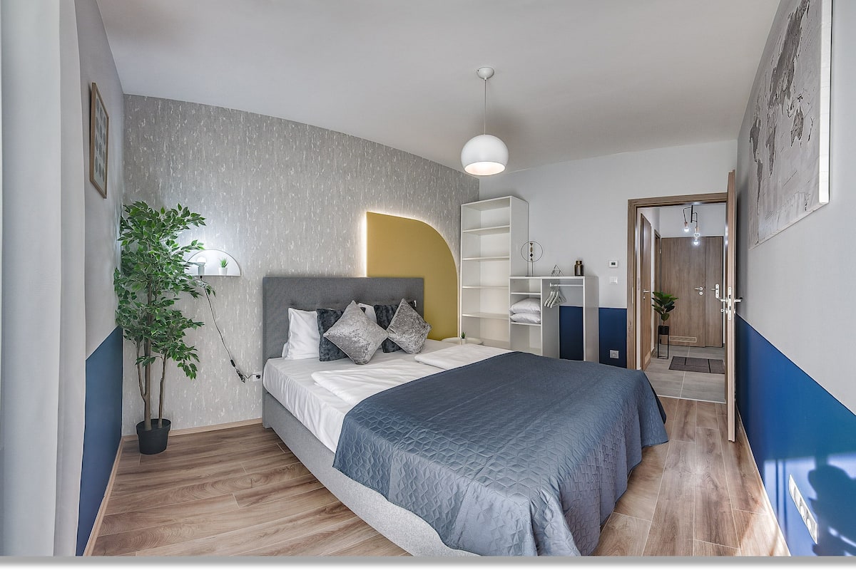 Un dormitorio moderno con cama, mesitas de noche, una planta en maceta y un armario.