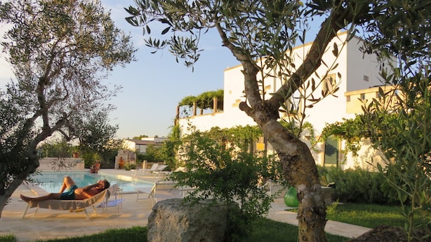 A pool area with lounge chairs, a person relaxing, and a building with a white facade and balconies.
