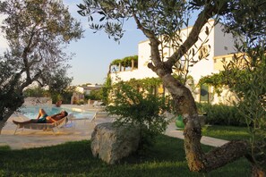 A pool area with lounge chairs, a person relaxing, and a building with a white facade and balconies. - Corte dei Salentini Bed & Breakfast (Carpignano Salentino)
