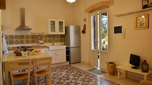 A kitchen with a tiled floor, a refrigerator, a stove, and a dining area with chairs and a table.