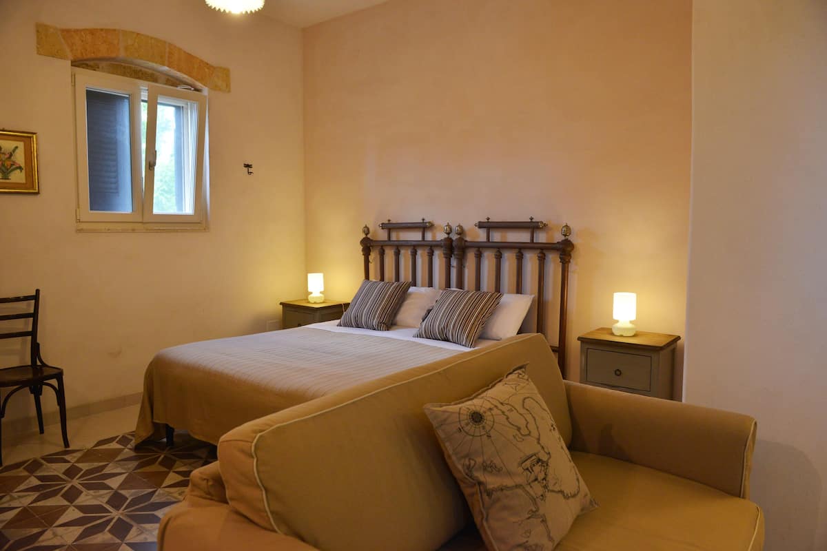 Une chambre à coucher avec un lit, deux tables de chevet avec des lampes, une chaise et un tapis à motifs.
