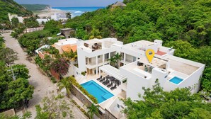 A modern resort with a pool, multiple balconies, and lush greenery. - Surfside Condo with Private Pool – 3 Minutes to the Beach (Huatulco)