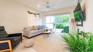 A modern living room with a sofa, a coffee table, and a TV mounted on the wall. - Surfside Condo with Private Pool – 3 Minutes to the Beach (Huatulco)