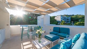 A sunlit outdoor patio with a pool, blue furniture, and a view of a building and trees. - Surfside Condo with Private Pool – 3 Minutes to the Beach (Huatulco)