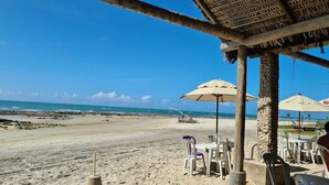 A beachside restaurant with outdoor seating, a thatched roof, and a view of the ocean. - Apartamento Luxo em Hotel - Beira Mar Fortaleza (Fortaleza)