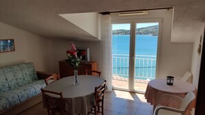Un coin repas avec une table et des chaises, un canapé, un téléviseur et une vue sur la mer, accessible par une porte coulissante.