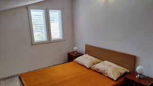 Une chambre avec un lit simple, deux tables de chevet, une fenêtre avec des stores et un luminaire fixé au mur.
