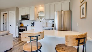 A modern kitchen with white cabinets, stainless steel appliances, a wooden dining table, and two chairs. - Your Private Inlet Beach Escape Awaits-Top Floor, Gulf Views, Community Pool (Inlet Beach)