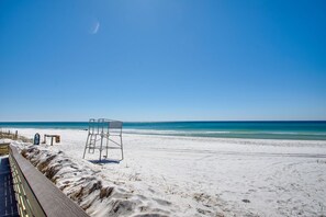 A beach with a lifeguard tower, a wooden boardwalk, and a clear blue sky.