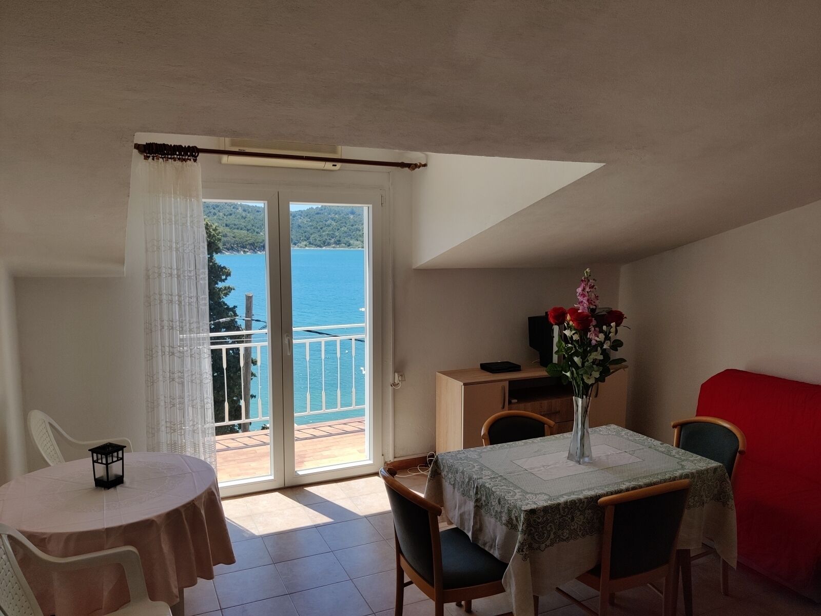 A balcony with a view of a body of water, a dining table with chairs, and a small table with a vase of flowers.