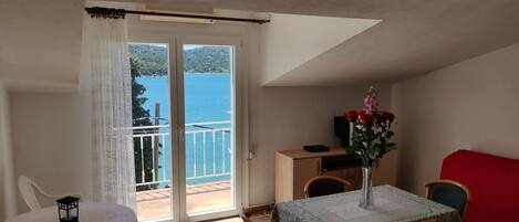 A balcony with a view of a body of water, a dining table with chairs, and a small table with a vase of flowers.