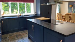 A modern kitchen with dark blue cabinets, a large island, and a window with a view of greenery. - The Bridge House, Dunbar including hot tub (Dunbar)