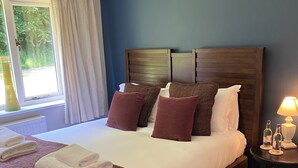 A neatly made bed with white and brown linens, a dark wooden headboard, and a bedside table with a lamp and bottles. - The Bridge House, Dunbar including hot tub (Dunbar)